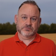 Unsmiling man with dark, thinning hair and salt-and-pepper facial hair